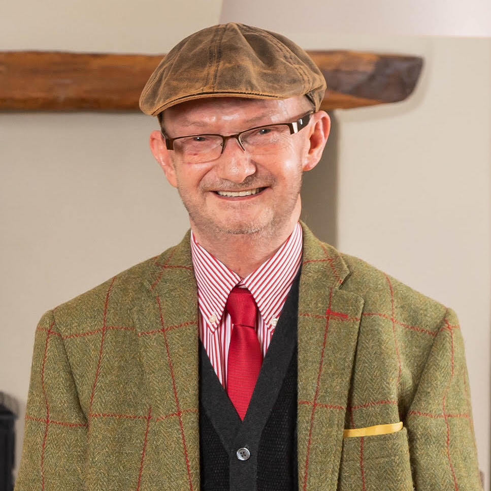 Grant smiling into the camera wearing a flatcap and green checked blazer